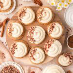 Carrot cake cookies with cream cheese frosting and chopped pecans arranged on a wooden board.