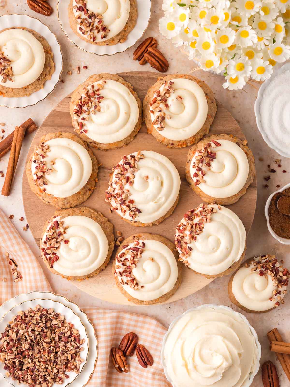 Carrot cake cookies with cream cheese frosting and chopped pecans arranged on a wooden board.