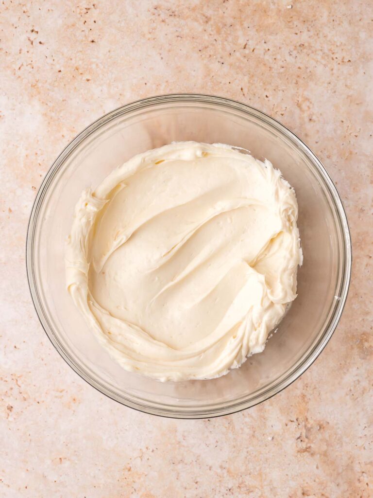 Smooth cream cheese frosting in a glass bowl ready for carrot cake cookies.