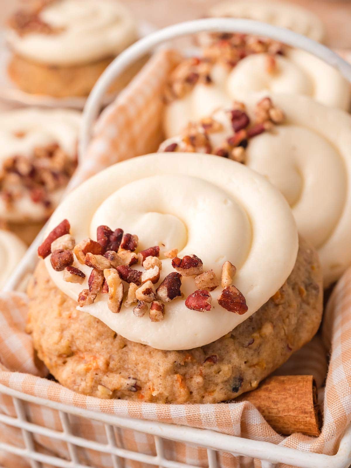 Carrot cake cookies stacked in a basket with cream cheese frosting and pecans.