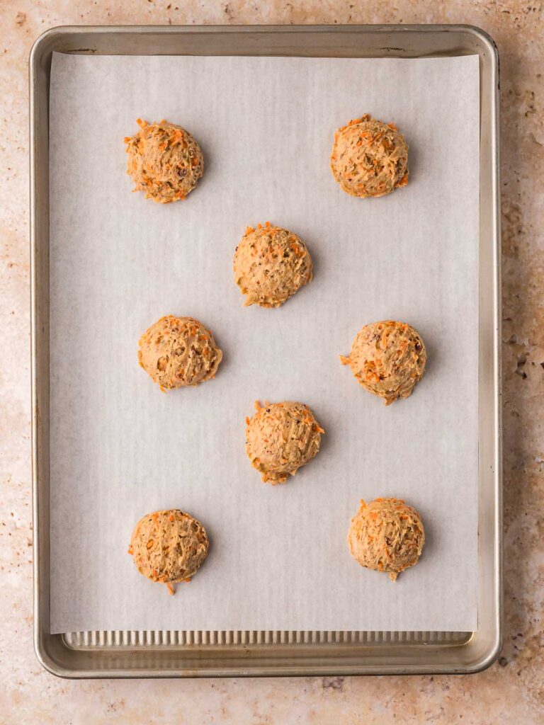 Carrot cake cookie dough scooped onto a parchment lined baking sheet before baking.