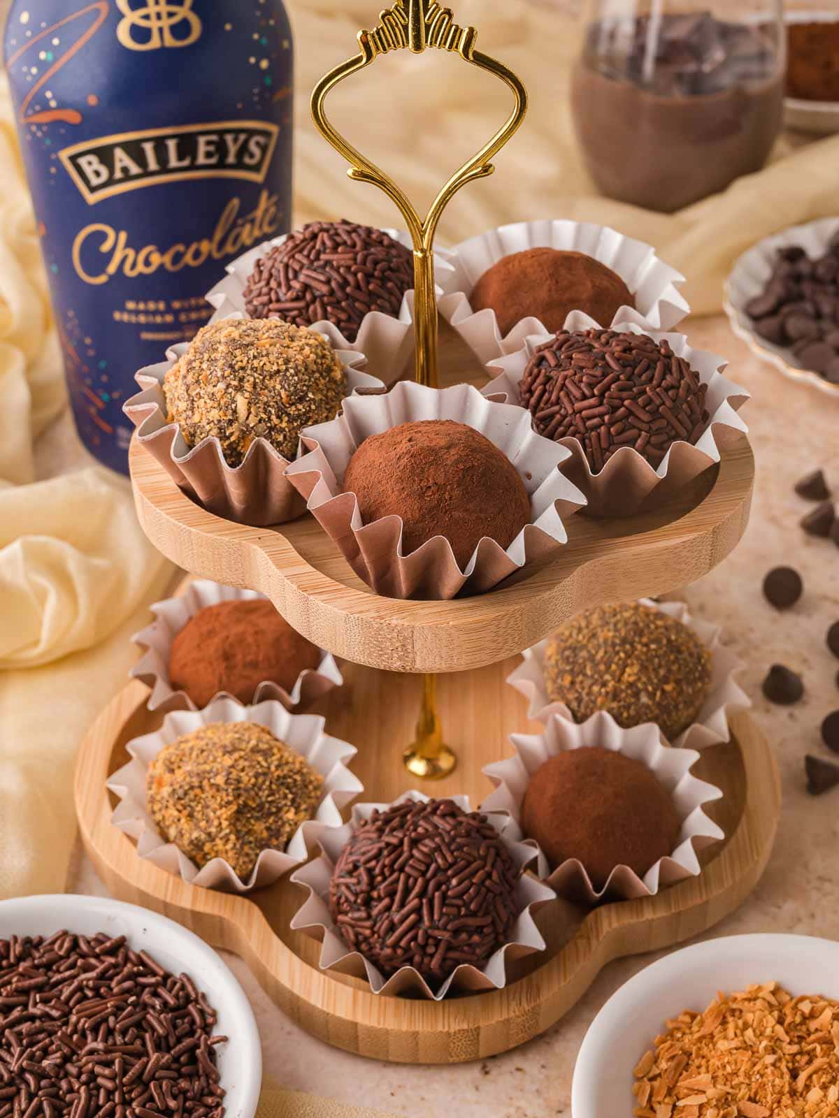 Chocolate Baileys truffles on a wooden dessert stand coated in cocoa powder, chocolate sprinkles, and nut topping.