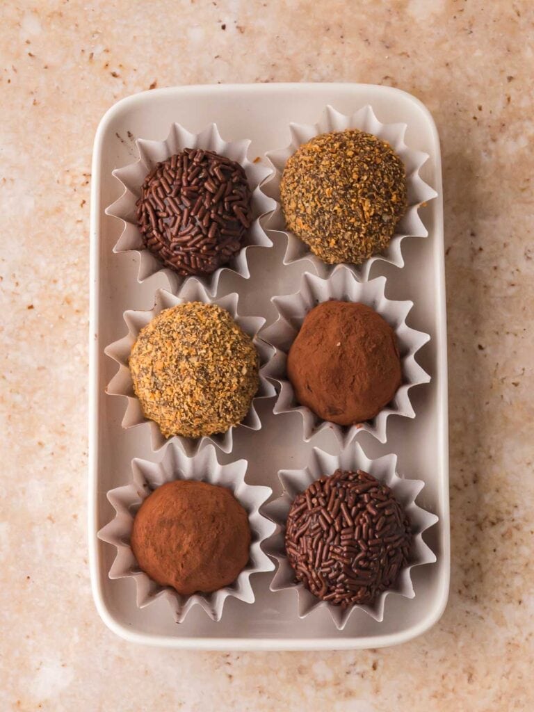 Chocolate Baileys truffles in paper cups coated in cocoa powder, chocolate sprinkles, and coconut topping.