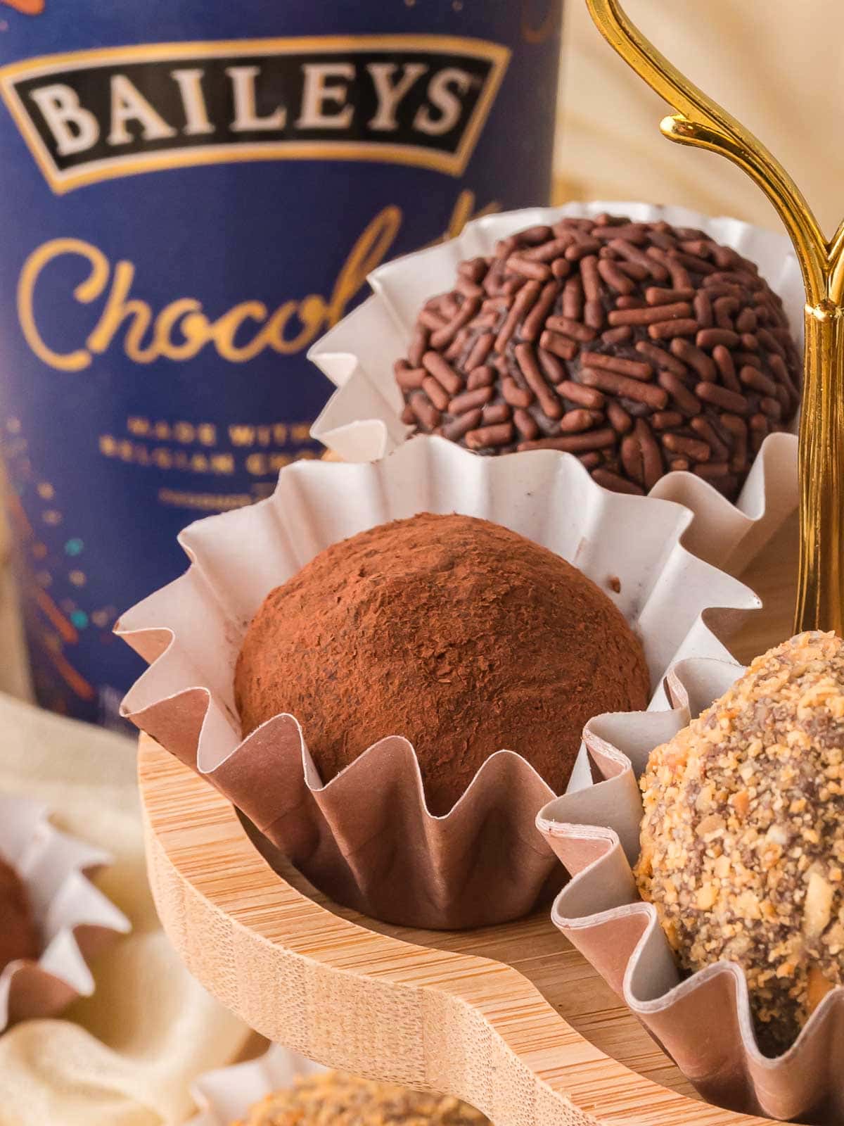 Close up of chocolate Baileys truffle coated in cocoa powder with Baileys chocolate liqueur bottle in background.