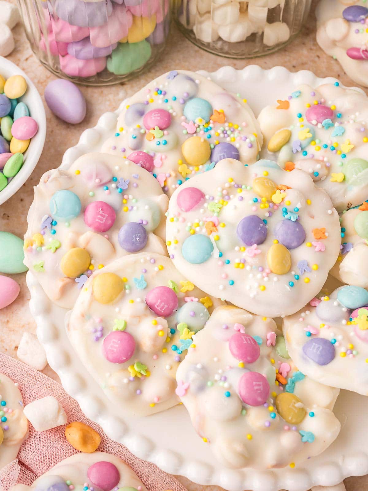 Overhead view of Easter candy clusters on a white platter with sprinkles and pastel M and M’s.