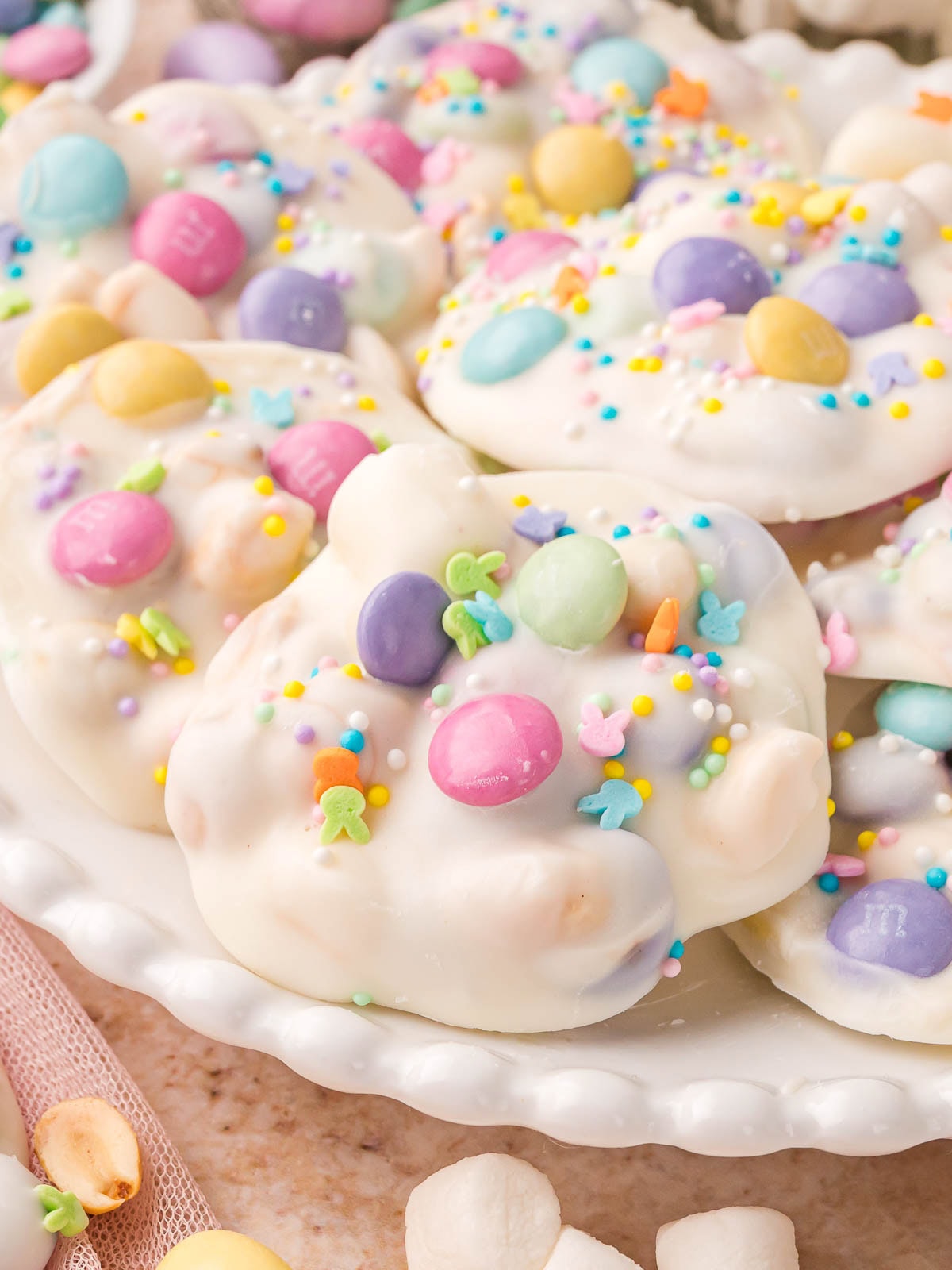 Crockpot Easter candy clusters coated in white chocolate with pastel M and M’s and sprinkles on a serving plate.