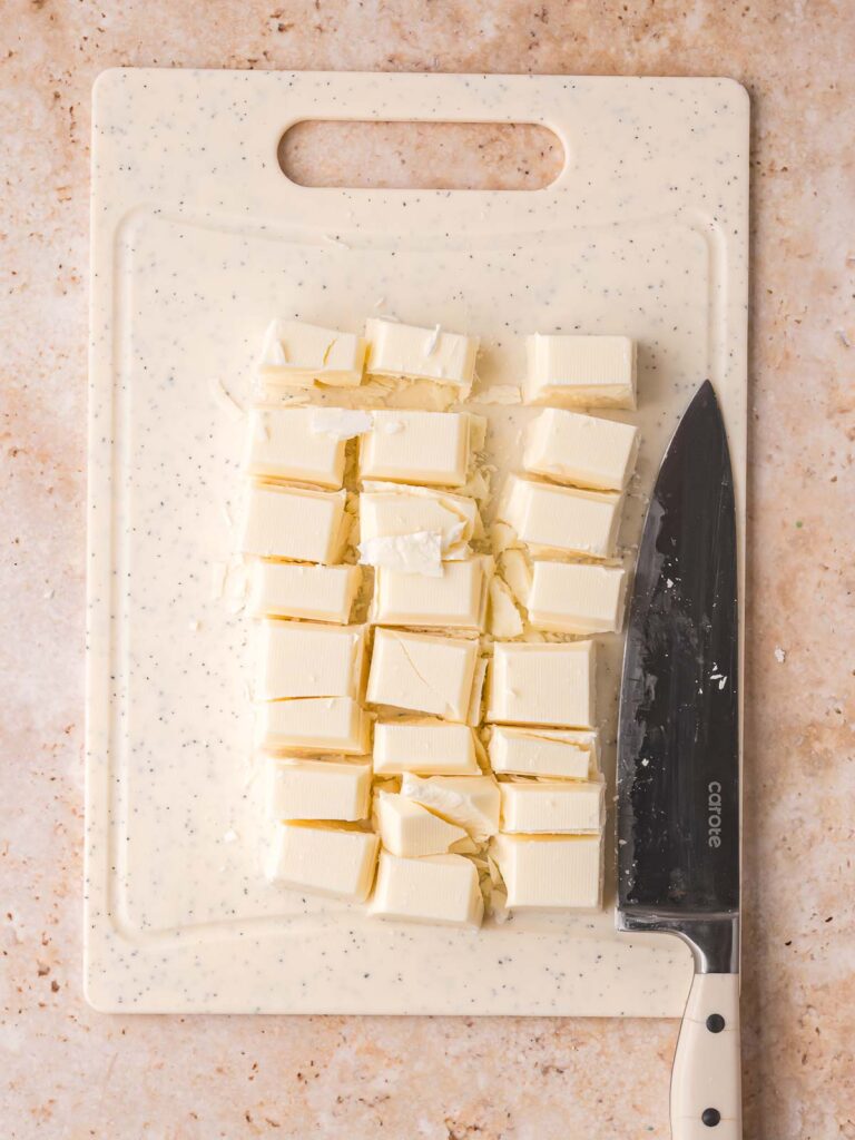 Chopped white almond bark on a cutting board with a knife ready for the slow cooker.