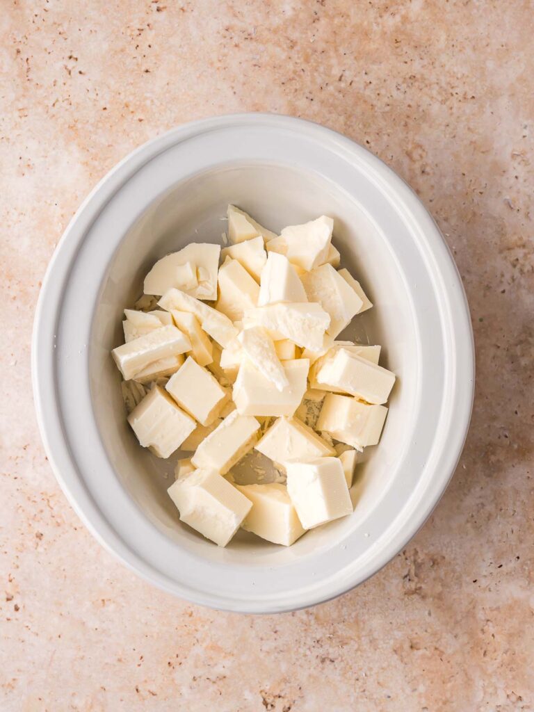 Chunks of white almond bark placed in a slow cooker before melting.