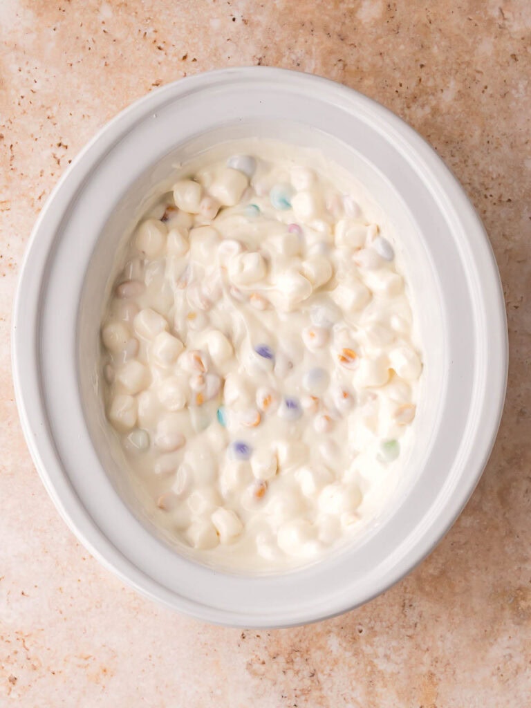 Melted white chocolate mixture with marshmallows and candy in a slow cooker.