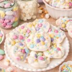 Plate of Crockpot Easter candy clusters surrounded by jars of marshmallows and pastel candies.