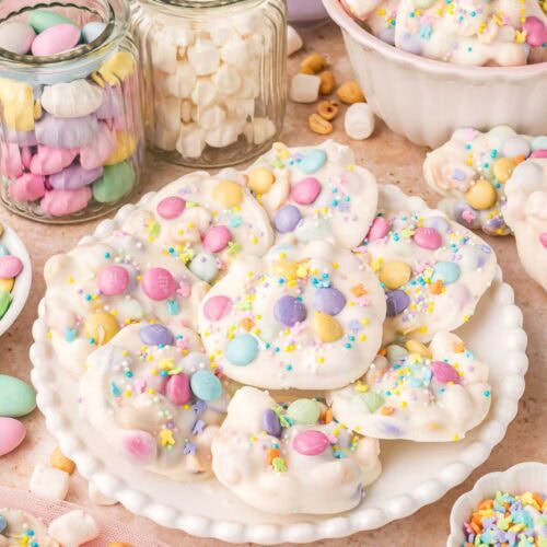 Plate of Crockpot Easter candy clusters surrounded by jars of marshmallows and pastel candies.