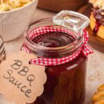 Homemade BBQ sauce in glass jar with ribbon label on table.
