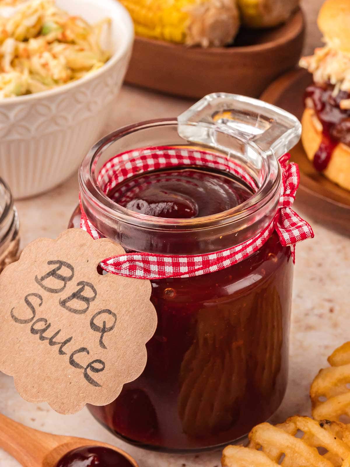 Homemade BBQ sauce in glass jar with ribbon label on table.