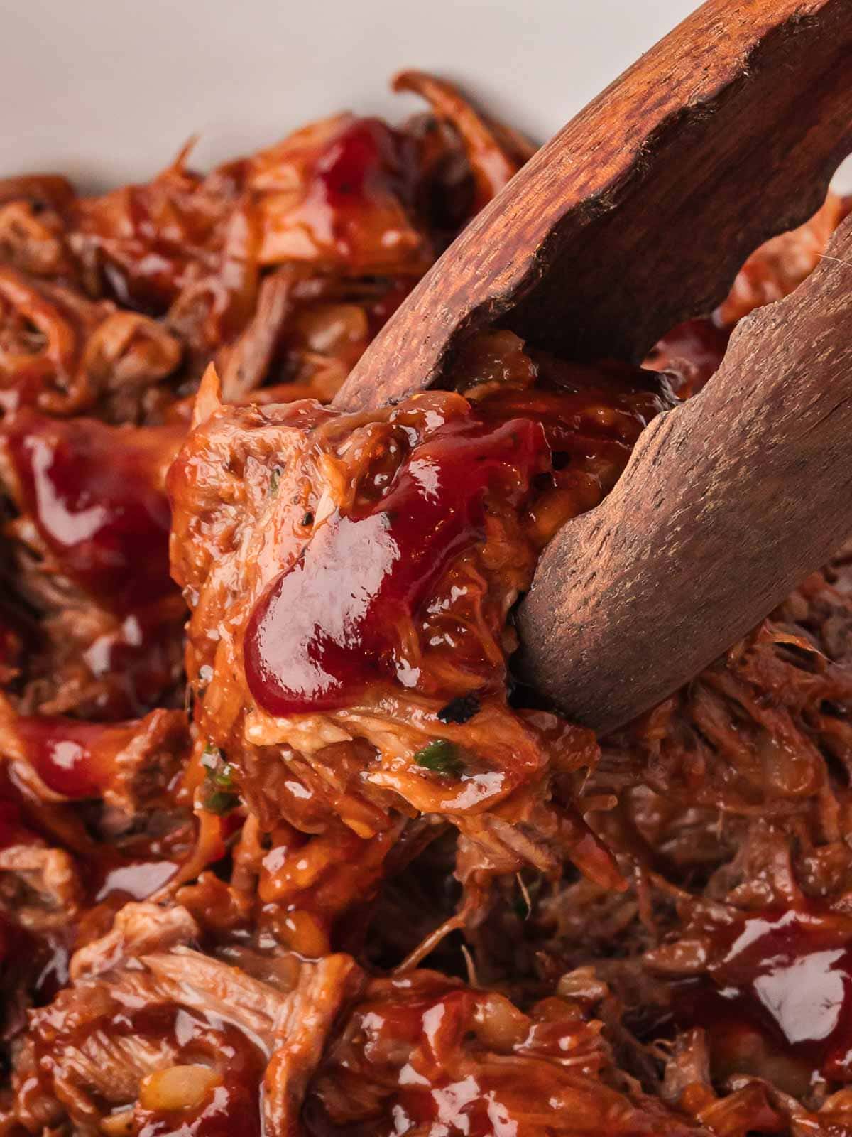 Tongs holding tender shredded BBQ beef in slow cooker.