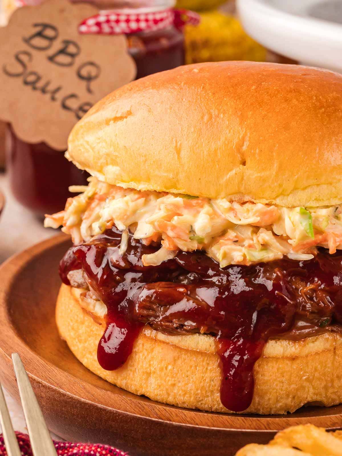 Close up of BBQ pulled beef sandwich with coleslaw and sauce dripping.