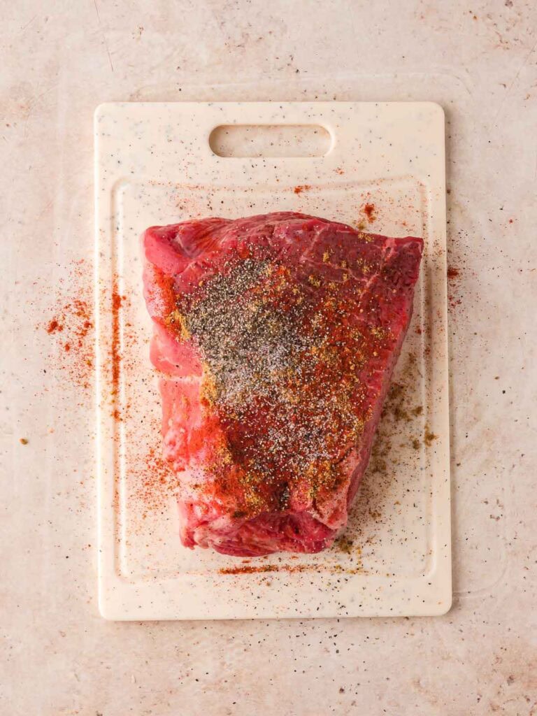 Raw chuck roast seasoned with spices on cutting board.