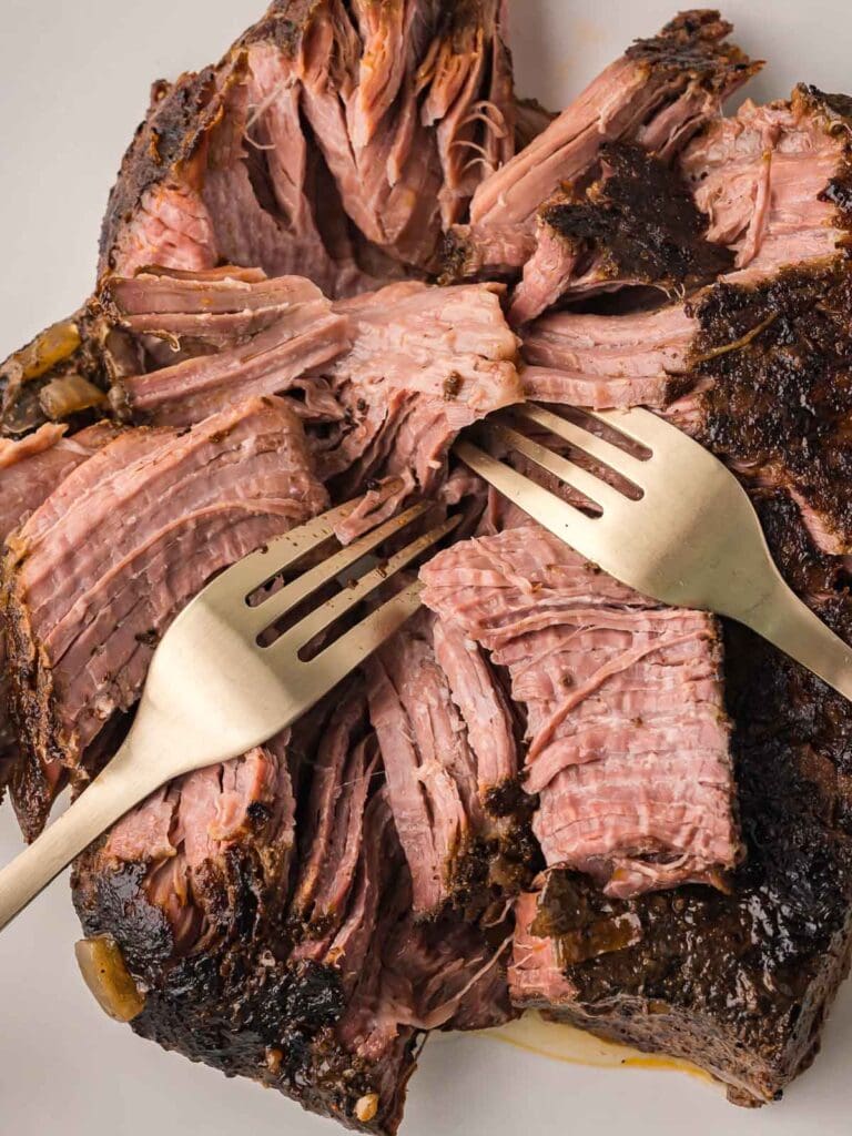 Cooked beef being shredded with forks after slow cooking.