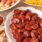 BBQ sausage bites served on a platter with pasta salad and grilled corn.
