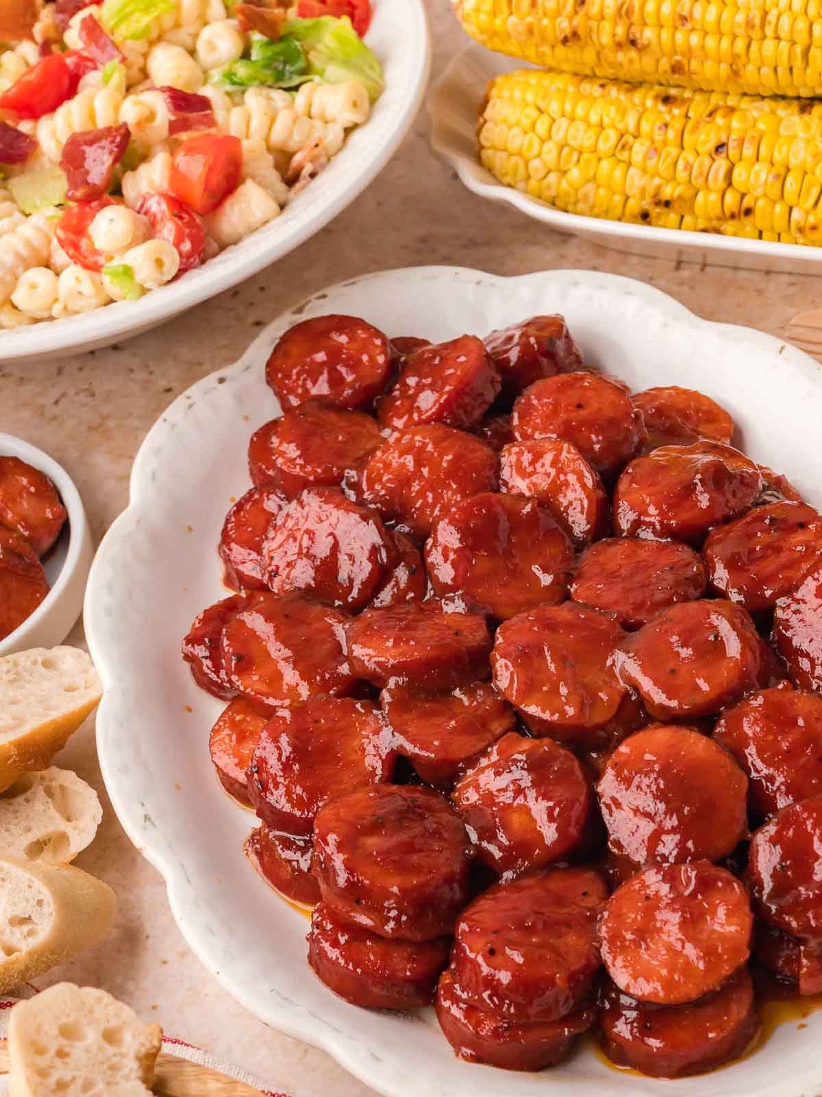 BBQ sausage bites served on a platter with pasta salad and grilled corn.