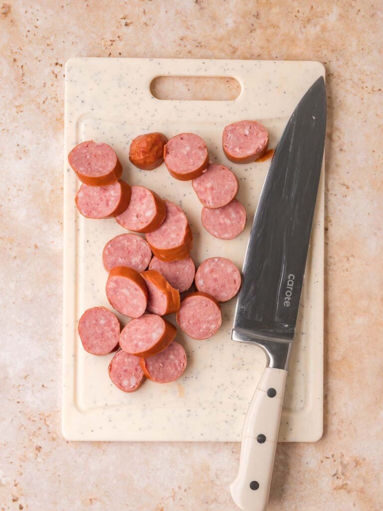Sliced smoked sausage on a cutting board with a knife for BBQ sausage bites.