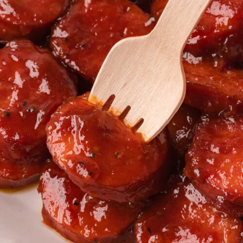 Fork picking up a BBQ sausage bite coated in sticky BBQ sauce.