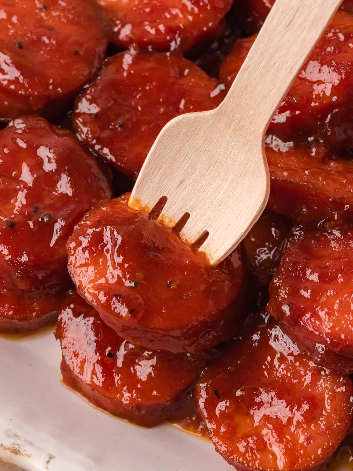 Fork picking up a BBQ sausage bite coated in sticky BBQ sauce.