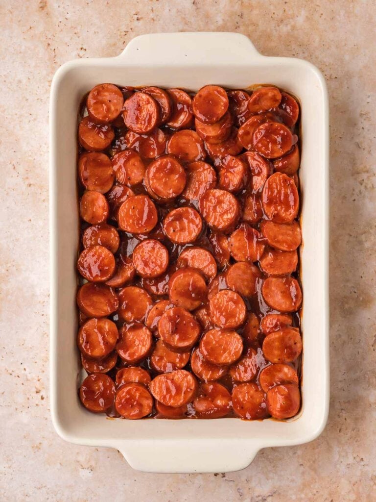 BBQ sausage bites coated in sauce arranged in a baking dish before baking.