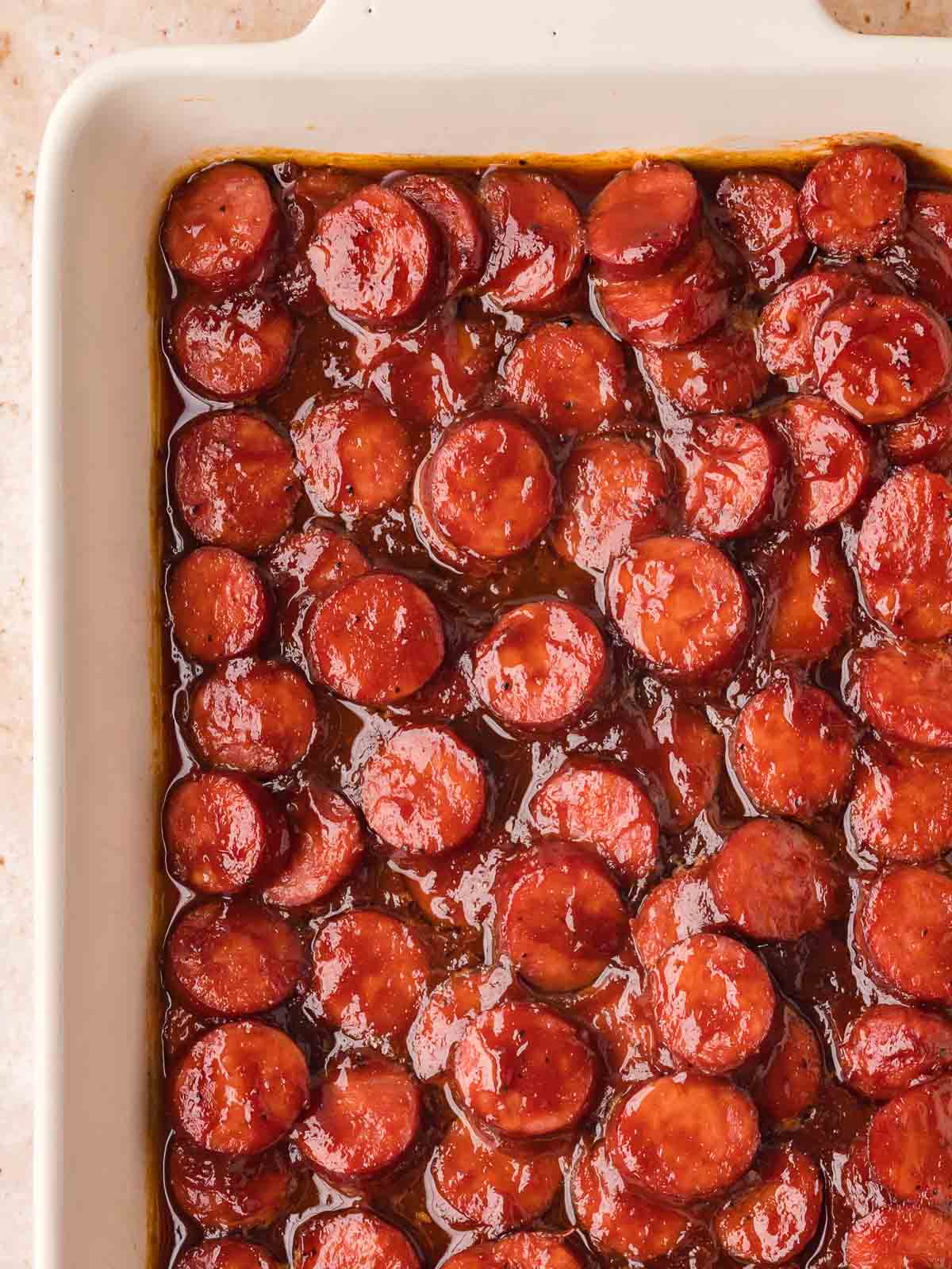 BBQ sausage bites in a baking dish with thickened sauce and caramelized edges.