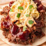 Slow cooker BBQ beef taco topped with creamy coleslaw, fresh cilantro, and BBQ sauce on a soft tortilla.