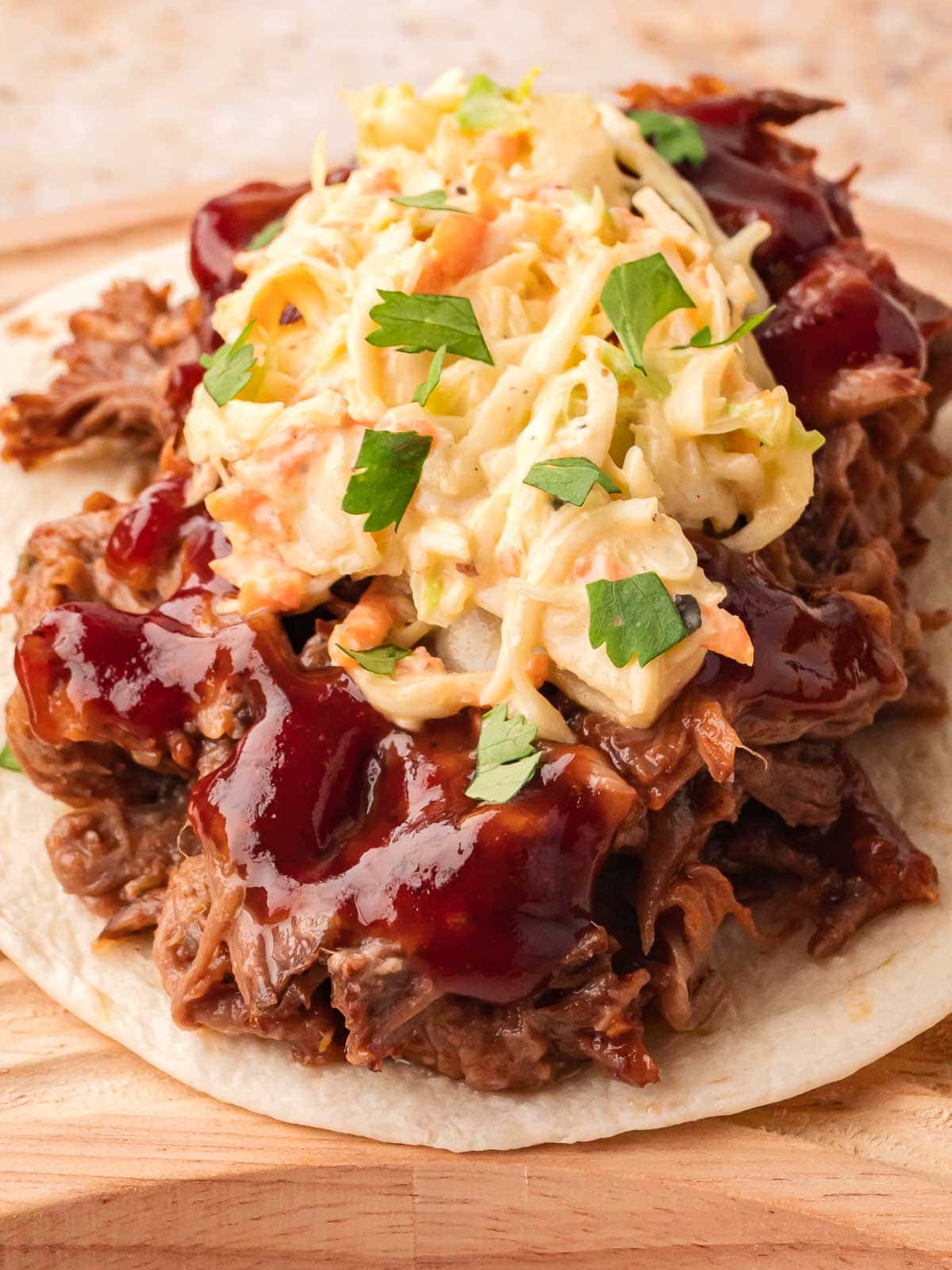 Slow cooker BBQ beef taco topped with creamy coleslaw, fresh cilantro, and BBQ sauce on a soft tortilla.