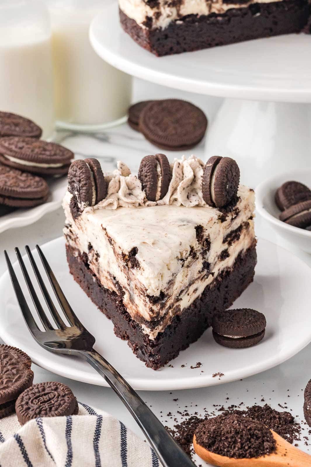 Oreo cheesecake slice on a plate with brownie base, Oreo whipped topping, and cookies on top.