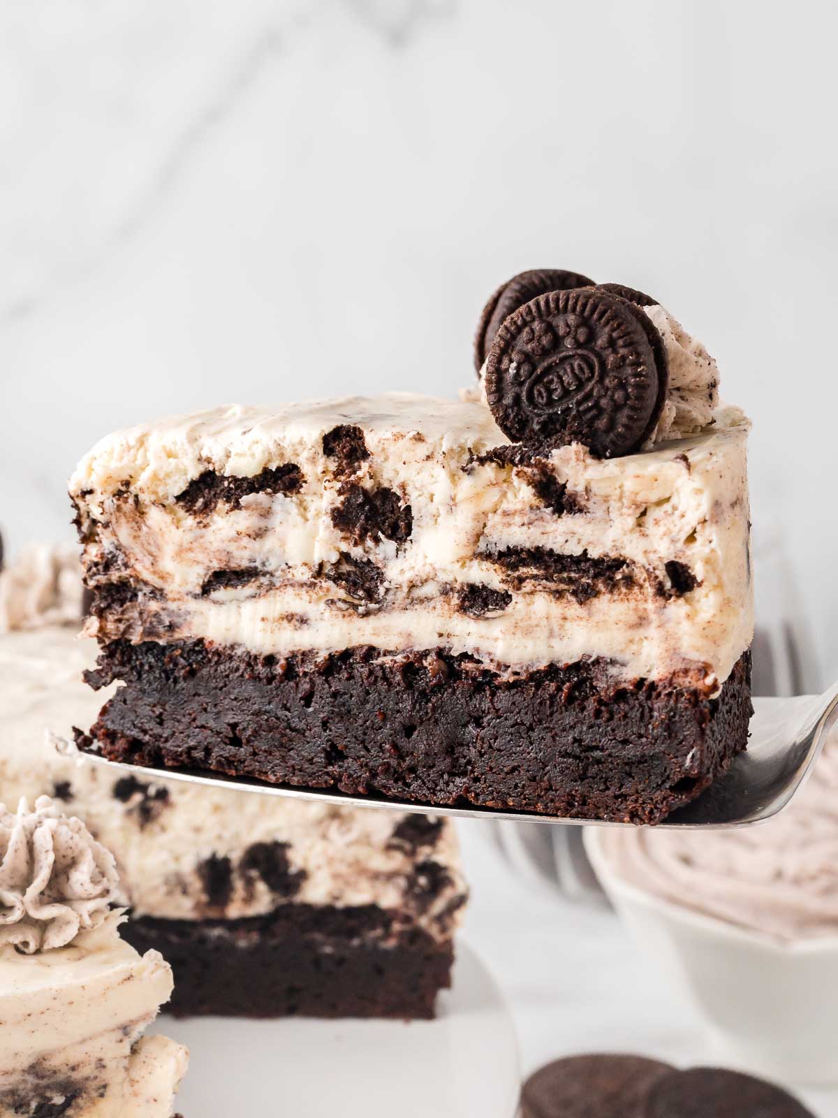 Slice of Oreo cheesecake with brownie base showing layers of creamy filling and chocolate brownie crust.