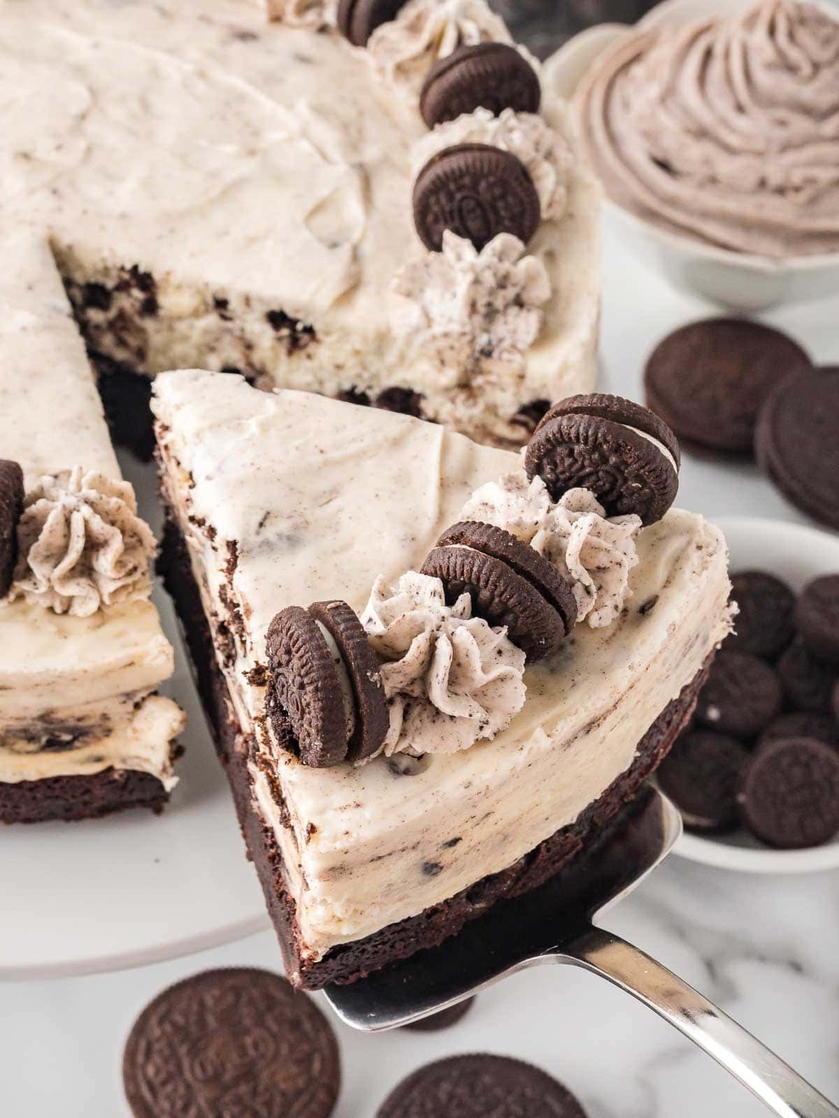 Oreo cheesecake slice being lifted with a spatula, showing thick brownie base and cookies and cream filling.