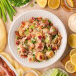 Creamy potato salad with bacon, celery, and green onions served in a bowl with fresh ingredients around it.