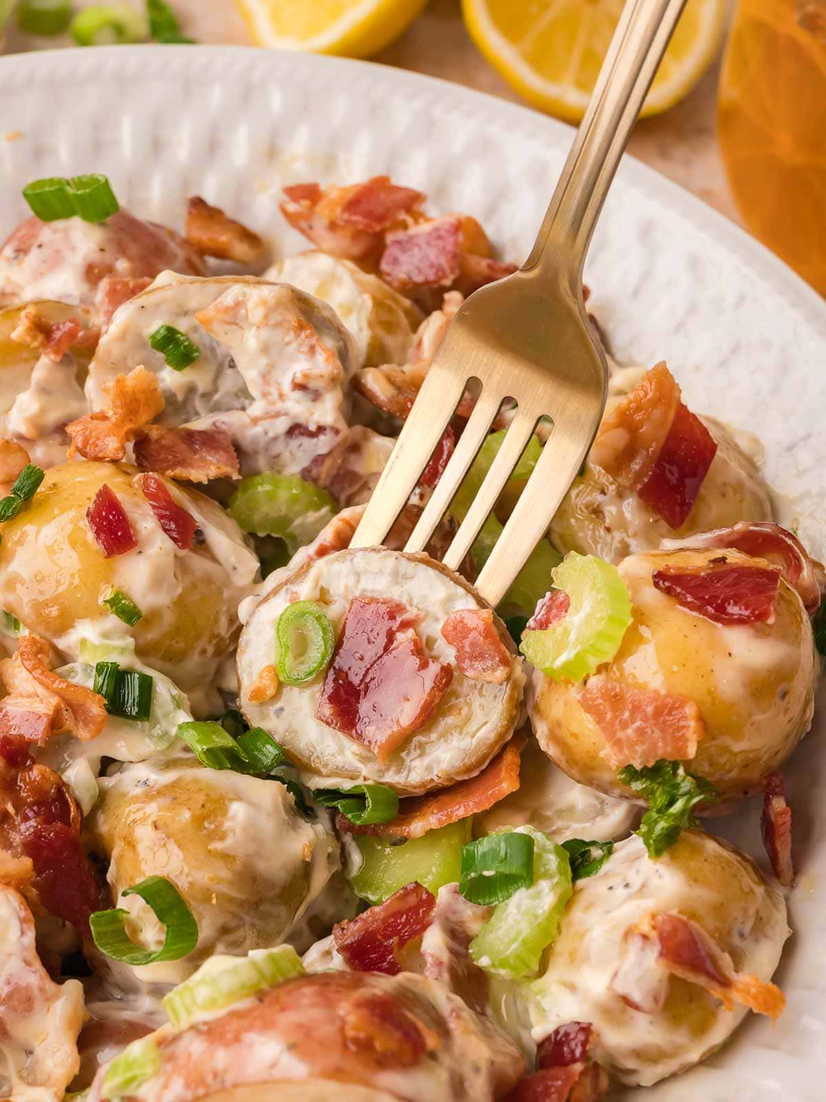 Fork lifting a piece of potato salad with bacon, celery, and creamy dressing from a bowl.