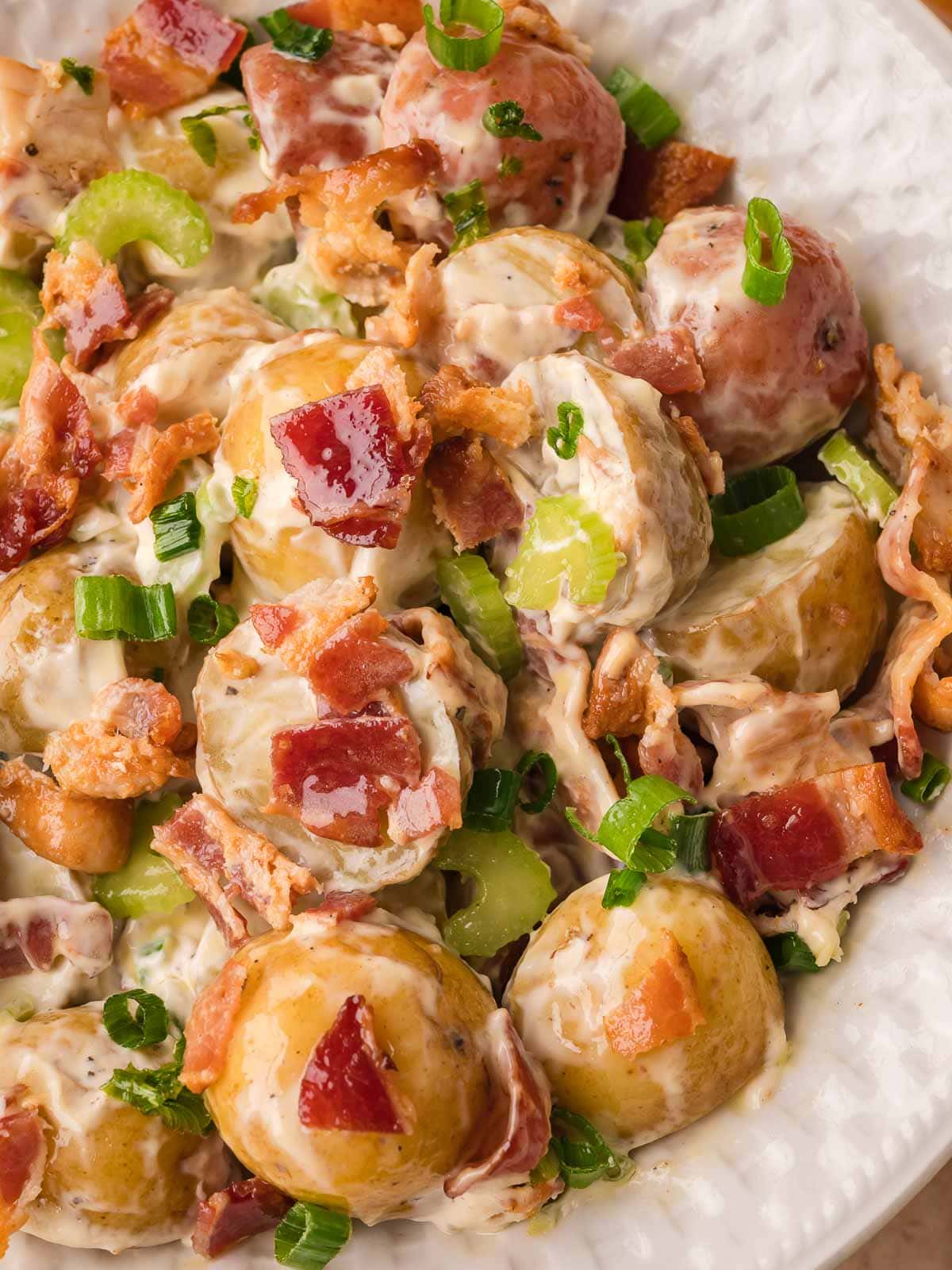 Close-up of potato salad with bacon, celery, and green onions coated in creamy dressing.