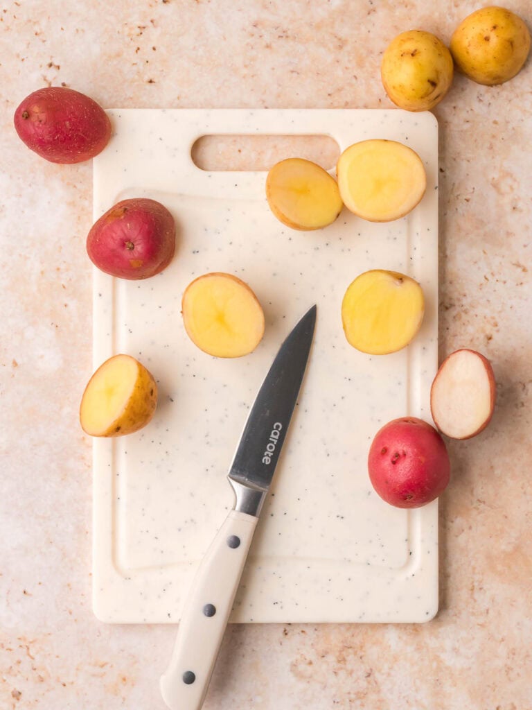 Cut baby potatoes in half on a cutting board with a knife for potato salad preparation.