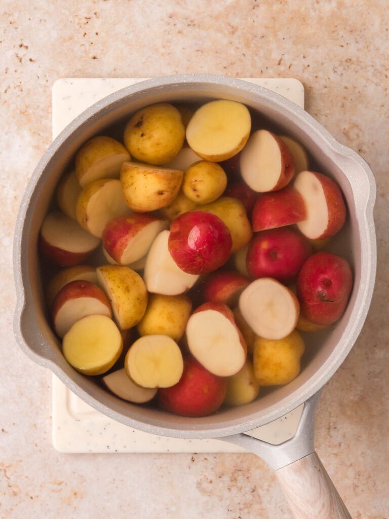 Halved baby potatoes soaking in a pot of water before boiling.