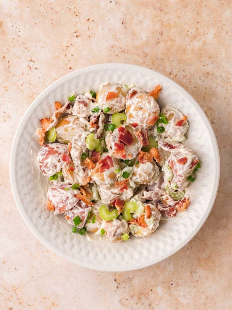 Creamy potato salad with bacon, celery, and green onions served in a bowl.