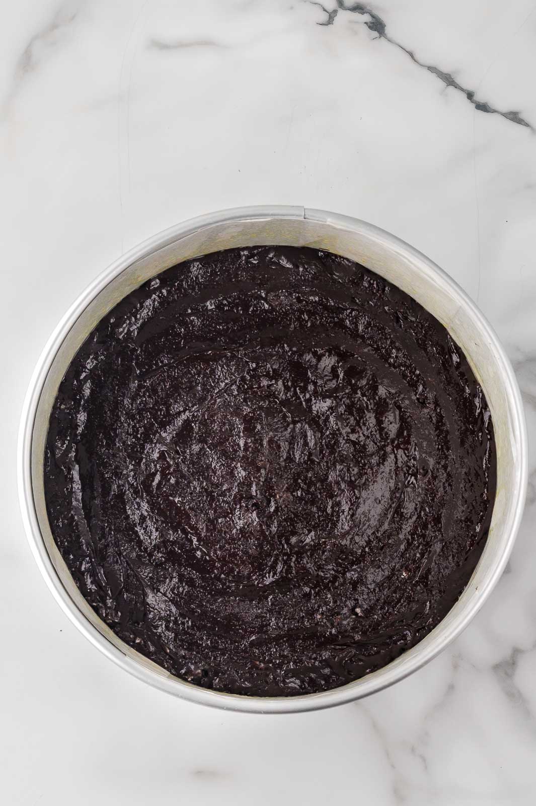 Baked brownie base spread evenly in a round pan for the Oreo cheesecake crust.