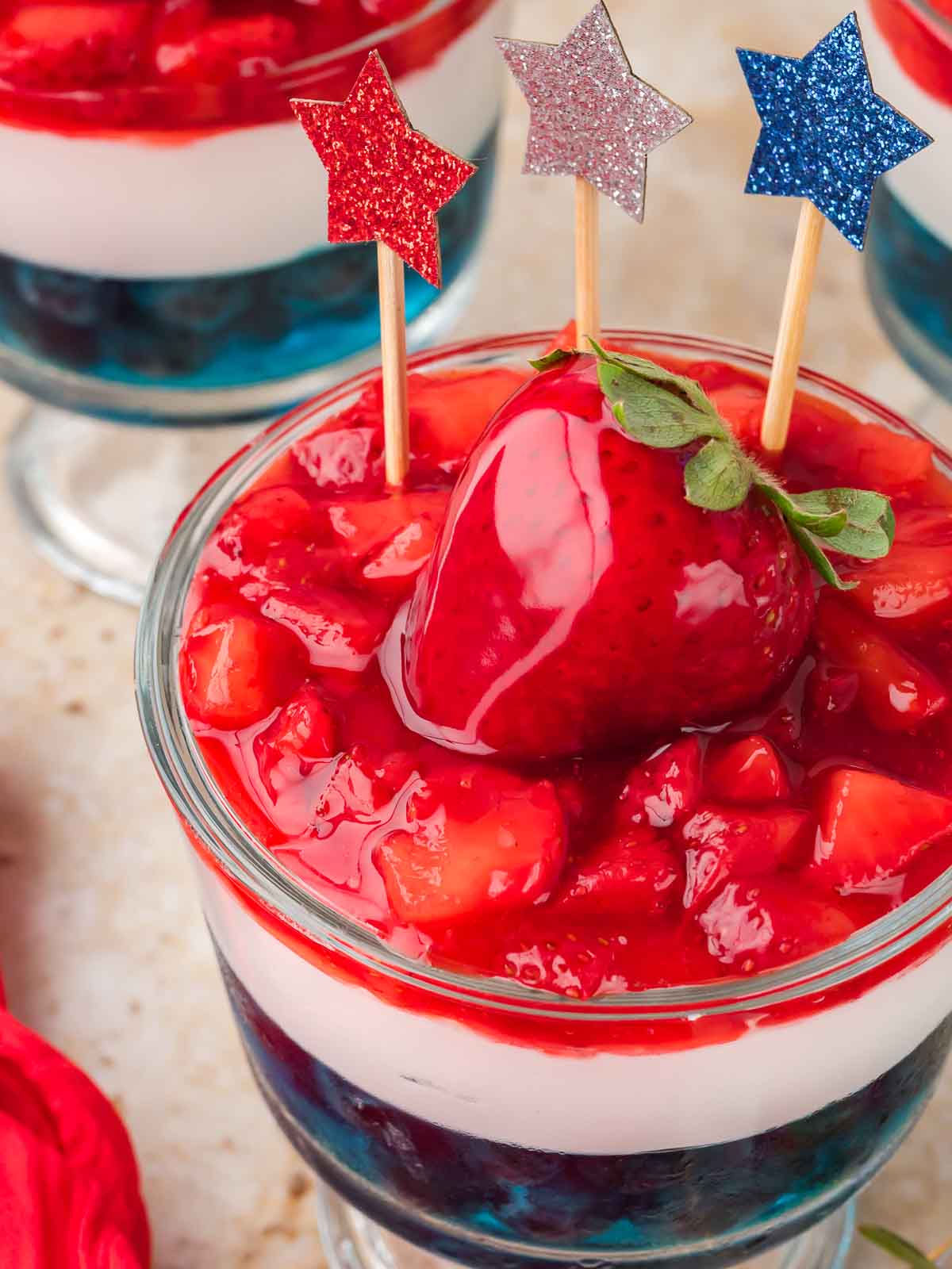 Close up of a Red White and Blue Dessert Cup with glazed strawberries and decorative star picks.