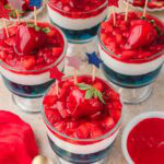 Red White and Blue Dessert Cups topped with glazed strawberries and red white and blue star picks on a countertop.