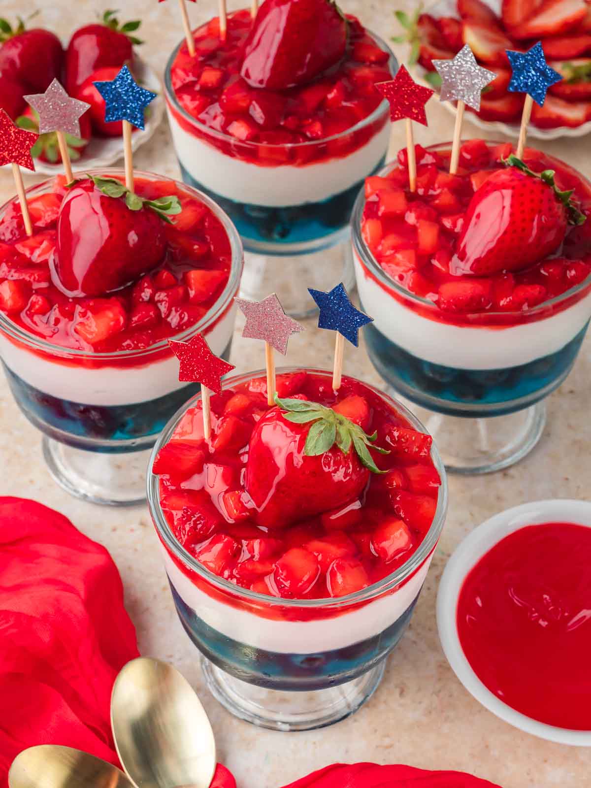 Red White and Blue Dessert Cups topped with glazed strawberries and red white and blue star picks on a countertop.
