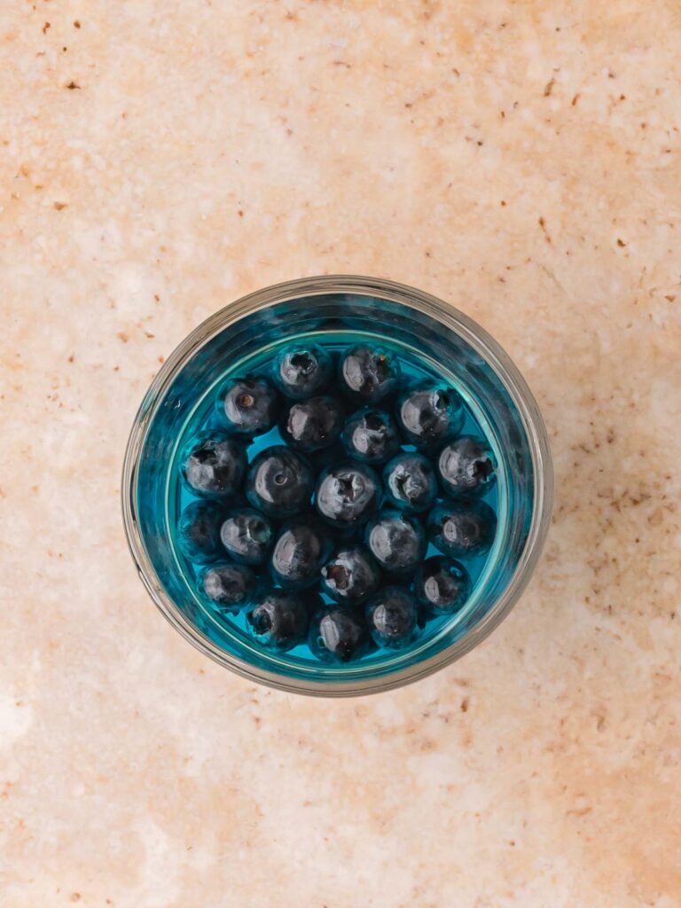Fresh blueberries sitting in blue Jello in a clear glass cup from above.