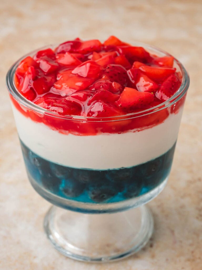 Red White and Blue Dessert Cup with blueberry Jello, Cool Whip, and glazed strawberries on top.