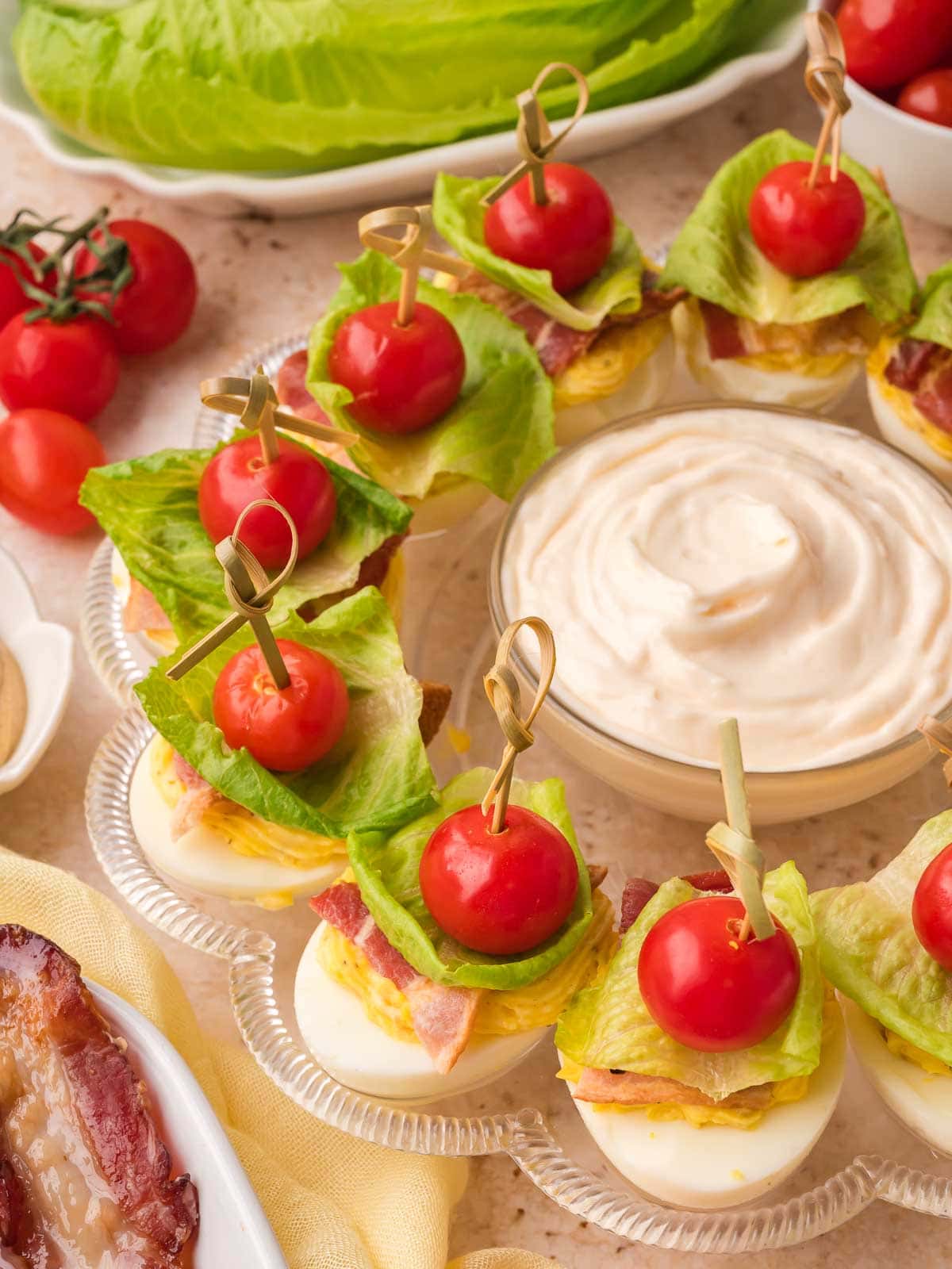 BLT deviled eggs topped with crispy bacon, lettuce, and cherry tomatoes served on a glass platter.