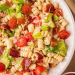 Creamy BLT pasta salad with bacon, lettuce, and cherry tomatoes in a white serving bowl.