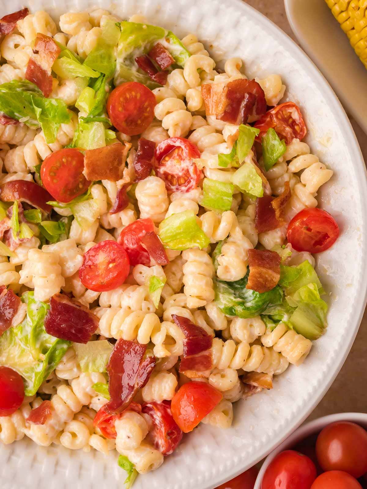Creamy BLT pasta salad with bacon, lettuce, and cherry tomatoes in a white serving bowl.