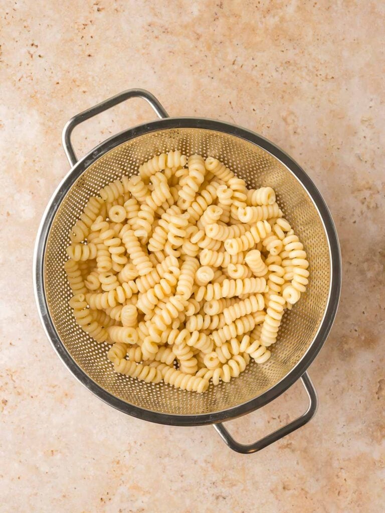 Cooked pasta draining in a metal colander.