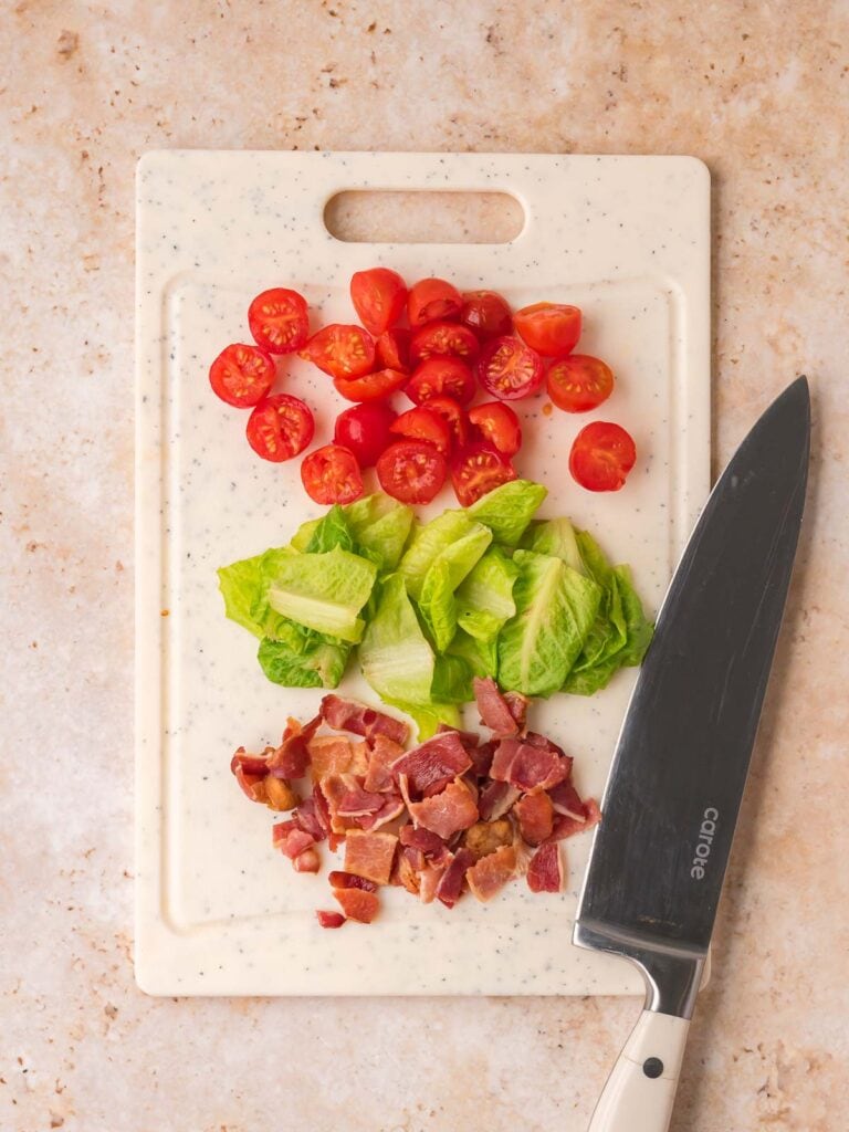 Chopped bacon, romaine lettuce, and cherry tomatoes on a cutting board.